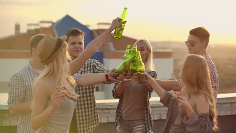 Russian-people-clinks-glasses-and-drinks-beer-from-green-bottels-on-the-party-with-friends-on-the-roof.-They-eat-hot-pizza-after.